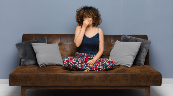 woman sitting on a couch and pinching her nose because of urine smell