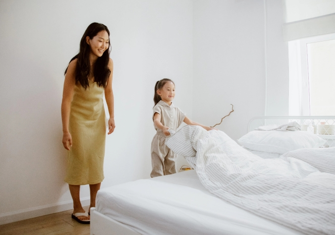 mom teaching her little girl to fix the bedsheets