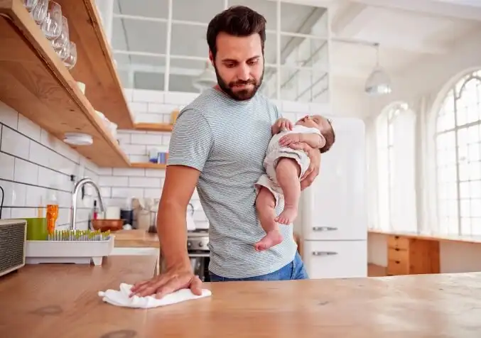 responsible father wiping the kitchen counter while taking care of a baby