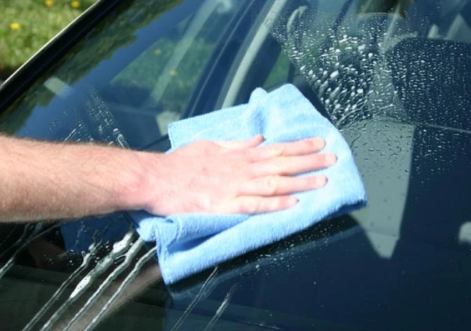 hand wiping a car windshield with a towel
