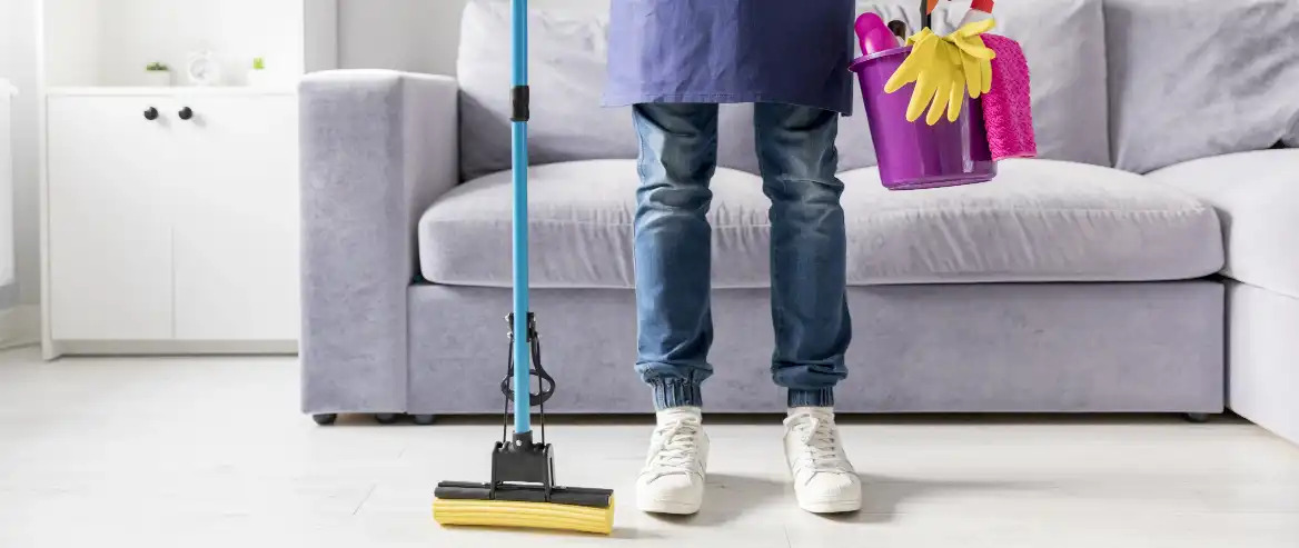 person holding a bucket of cleaning supplies standing in the middle of the living room