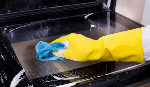 Applying baking soda paste inside oven for natural grease removal.