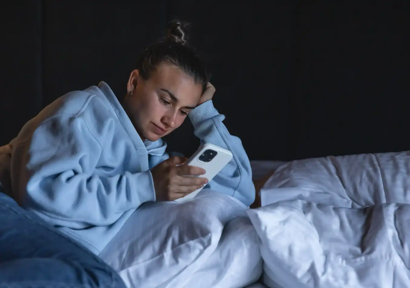 woman scrolling through her phone while in bed