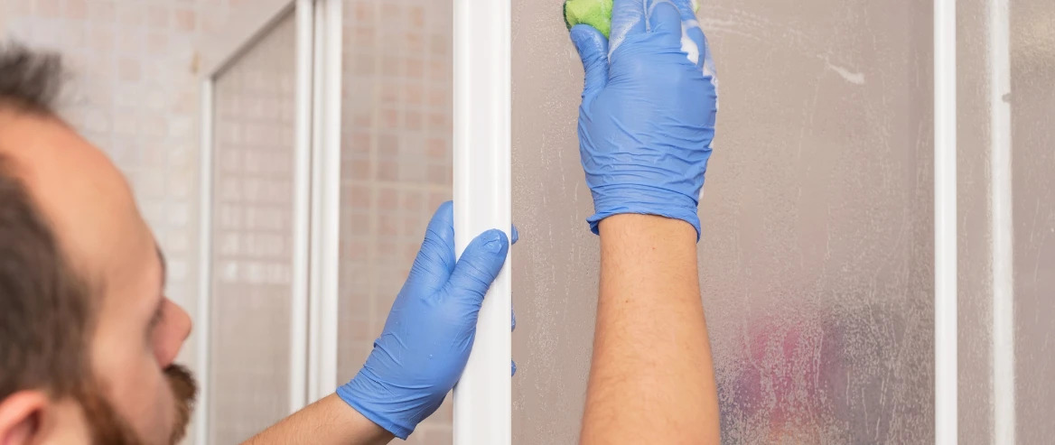 man removing soap scum from shower door