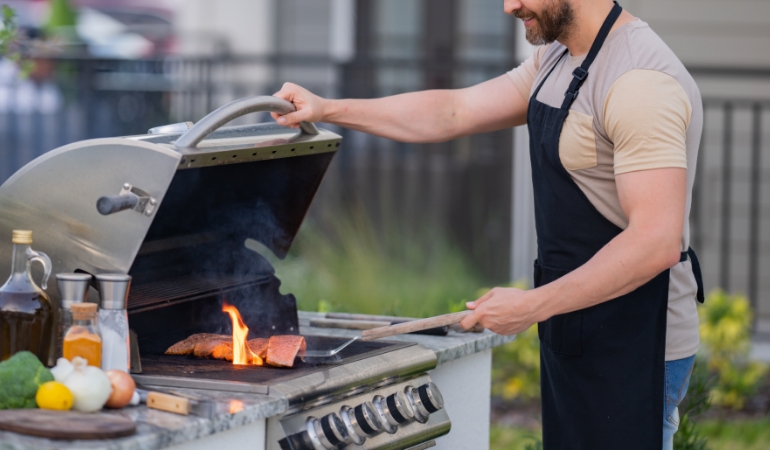 Cooking outdoors on a barbecue to reduce indoor heat and air conditioner load.