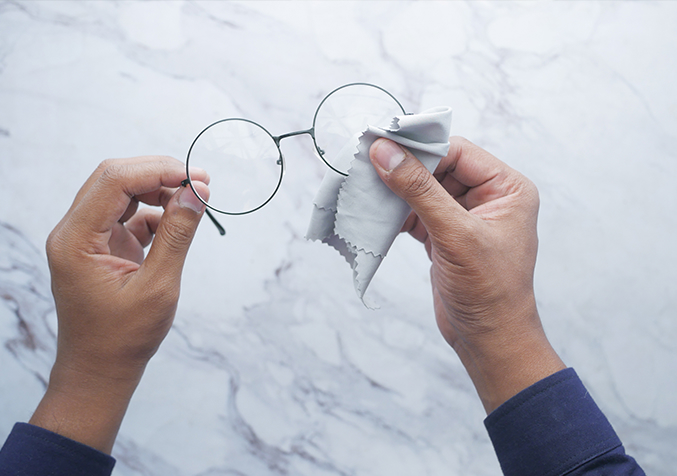 Cleaning eyeglass lenses with a soft cloth to minimise very fine surface marks.