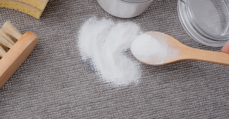 Sprinkling bi-carb soda on a fabric sofa to absorb odours before vacuuming