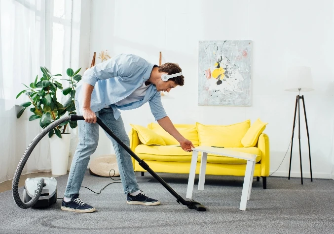 man vacuuming carpet underneath table