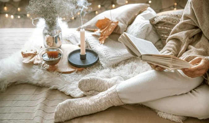 woman wearing socks and sweater reading book in a cozy and comfy bed