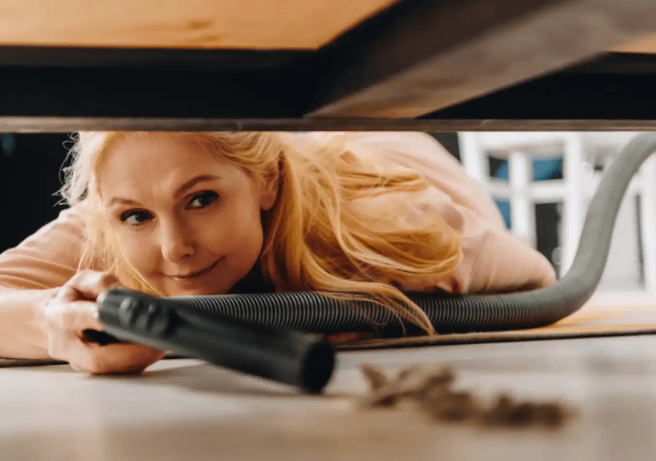 woman using the vacuum to clean below a furniture