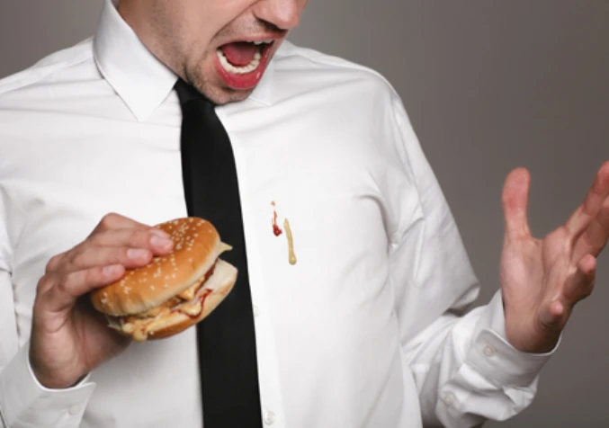 suprised man looking at food stains from his burger on his right hand