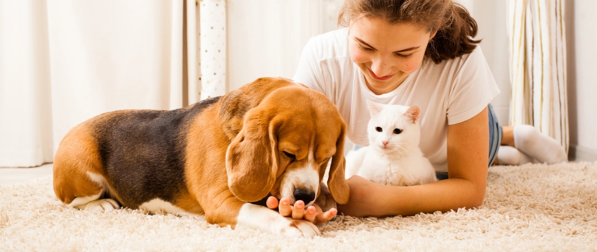 woman petting her cat and dog while laying on the carpet