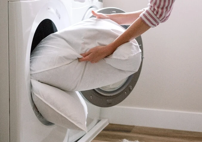 hand putting pillow inside washing machine