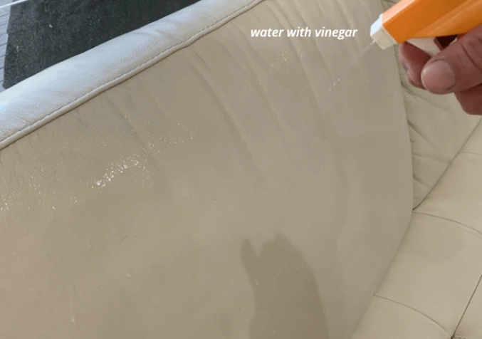 Spraying a white vinegar and water solution onto leather to remove soap residue.