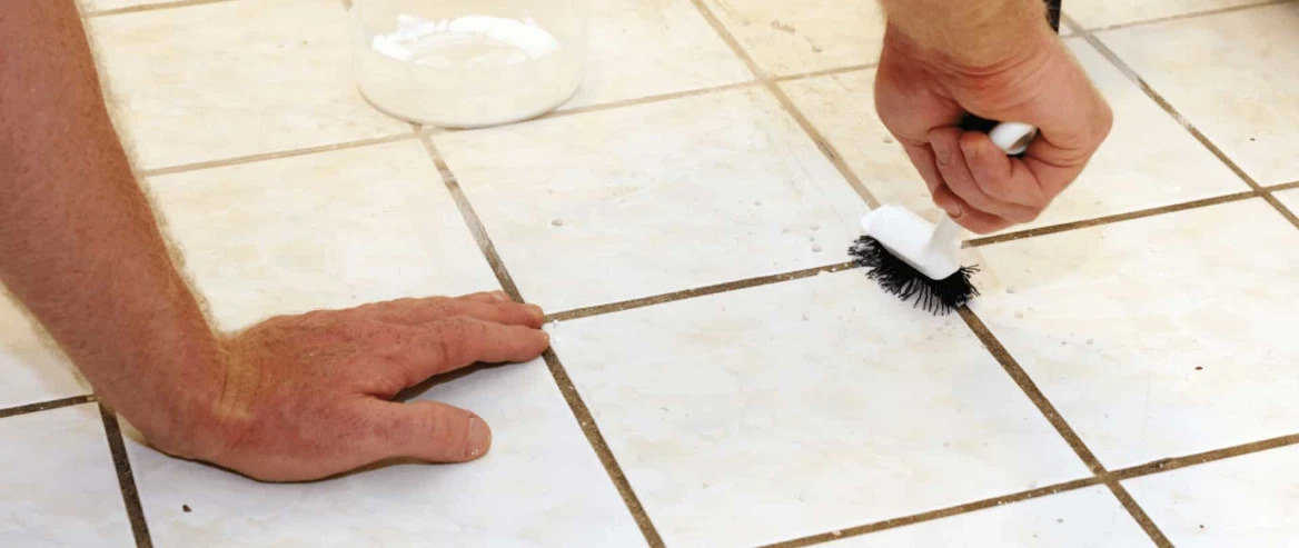 person on hands and knees scrubbing grout